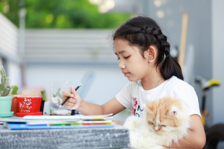 Portrait of a Little Asian girl doing homework and hugging her Persian cat with happiness, select focus shallow depth of fieldの写真素材