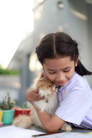 Portrait of a Little Asian girl in Thai student uniform is hugging her Persian cat with happiness, select focus shallow depth of fieldの写真素材