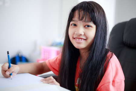Portrait shot little Asian girl doing homework to learn from home and smile with happiness, self-quarantine and self-education concept, selective focus shallow depth of fieldの写真素材