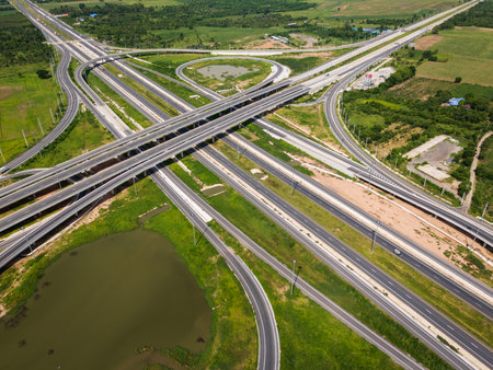 Drone shot a large highway interchange crossing over green farmlands in Thailand. The layered roads...