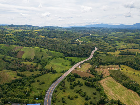 Aerial drone view of Highway winding through lush green mountains between Nan, Thailand. A scenic landscape of the road surrounded by tropical forest and a peaceful countrysideの写真素材