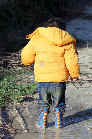 toddler boy having fun jumping in a muddy puddleの写真素材