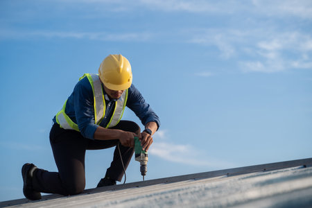 Worker repairing the roof on a construction site. Electric drill used on roof, Roof construction concept.の写真素材