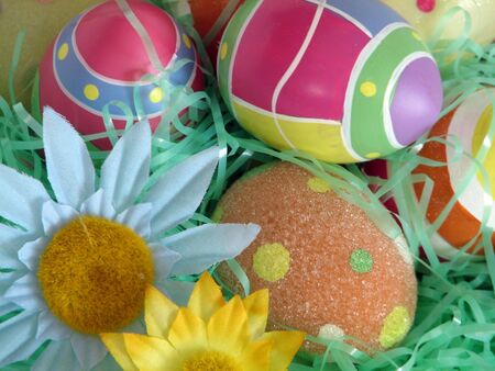 Closeup of several Easter eggs over green artifial grass and a couple flowers.