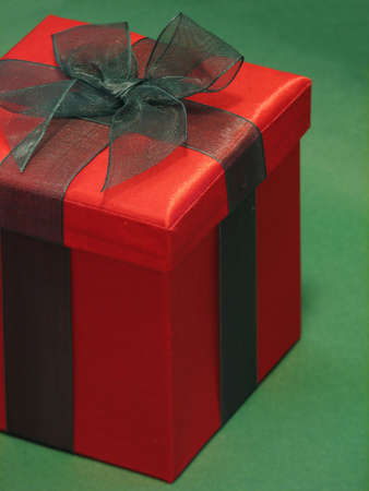 Shot of a red gift box with a green ribbon against a green background.