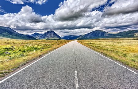 A long straight road leading towards a snow capped mountain in scotlandの写真素材