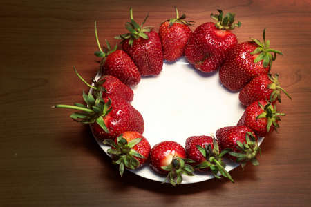 plate of bright and fresh red strawberries on a wooden countertop. top view, selective light on objectの写真素材