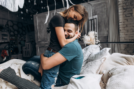 Loving couple hug each other on the bed, in big bedroom. Love story, side view