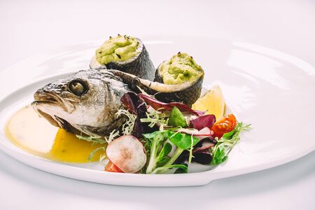 Baked trout with spinach puree, with herbs, tomatoes, lemon and sauce on round white plate. Side viewの写真素材