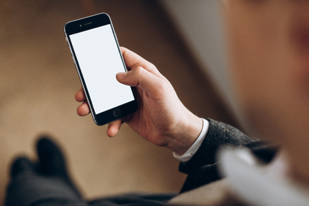 Male hand holds a smartphone with a clean white screen and space for text. Top viewの写真素材