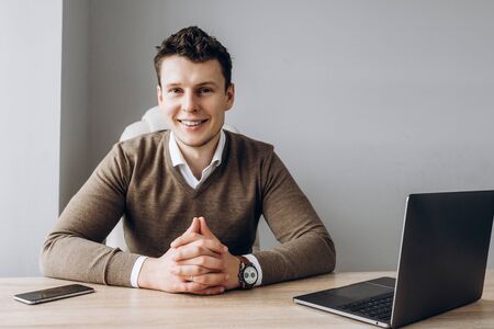 Portrait of a young handsome businessman who sits in his workplace in a positive mood