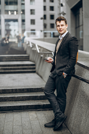 Image of an attractive businessman in a stylish suit with a smartphone in his hand and with a charming smileの写真素材