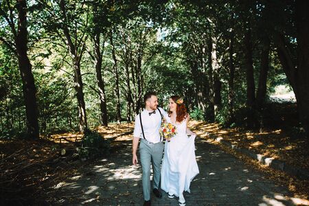 Newlyweds are walking in nature and laughing. The groom hugs his red brideの写真素材