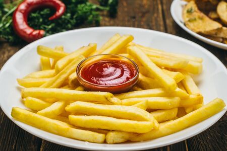 Crispy french fries on a white round plate with tomato sauce and parsley