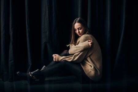 Young girl in stylish clothes is posing sitting on the floor indoors with a black backgroundの写真素材