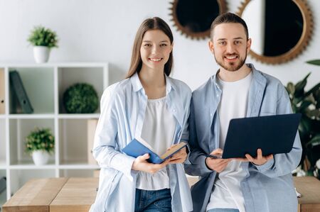 Business colleagues. A girl with a notebook in hands, a guy with a laptop, stand in his office and...