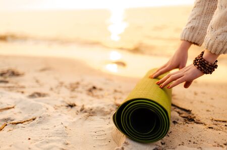 Female hands and yoga mat in the sand on the beach at sunset, close-upの写真素材