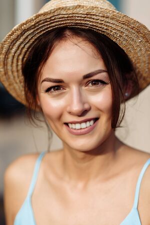 Feminine portrait of a beautiful young girl with a charming smile in a summer hat. Close-upの写真素材