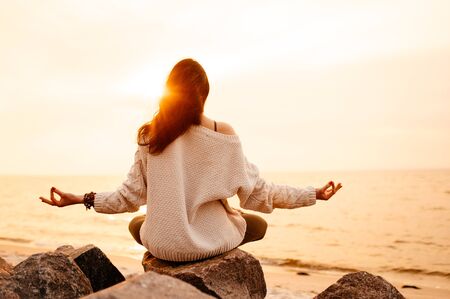 Inspirational photo of a girl who sitting in lotus position and meditates at sunset by the seaの写真素材