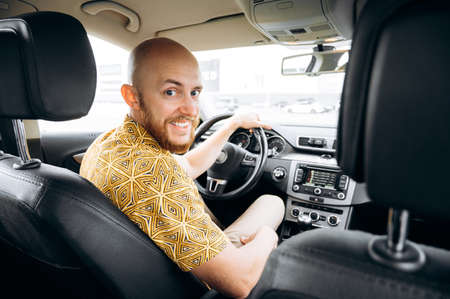 Positive bearded driver. Smiling man driver in casual wear sitting behind the wheel of his car looking at the camera and smilingの写真素材