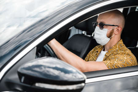 Quarantine. A man wearing a protective medical mask and sunglasses drives in his car to the shop during the quarantine of coronavirusの写真素材