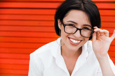 Female business portrait. Young attractive business woman in a white shirt and eyeglasses sits on a bench outdoors looks at the camera and smilingの写真素材