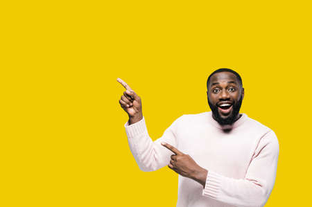 Smiling african american man points for finger on copy space for your advertising or text, with...