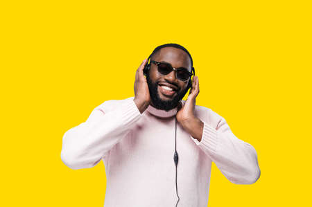 Smiling African American attractive man in eyeglasses enjoy of his favorite playlist in headphones,...