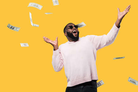 Cheerful happy african american man in sunglasses look up at falling money, winning lottery standing...