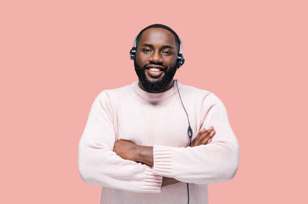 Handsome young african american man worker of a call-center with headphones is standing on a pink...