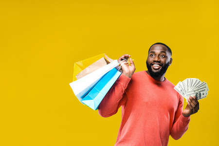 Shopping time. Cheerful african american man stands on a yellow background holds paper shopping bags...