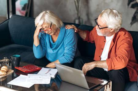 Online bill payment. Frustrated retirees count and pay utility bills. Husband calms his wife by putting his hand on her shoulderの写真素材