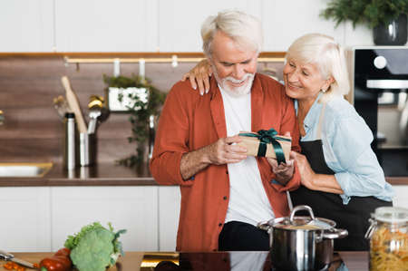 Happy mature couple in love. Caring wife gives a gift to her beloved husbandの写真素材