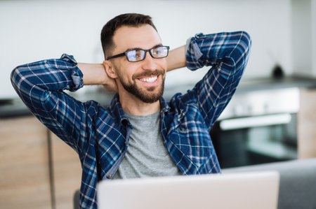 Positive freelancer guy relaxing at the workplace and smiling. Confident caucasian male entrepreneur sitting at home office, taking break from distant working and dreaming about vacationの写真素材