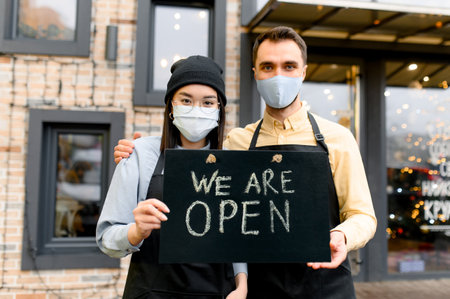 Welcome, we are OPEN. Two friendly waiters wearing protective masks. Multiracial waiters, caucasian...