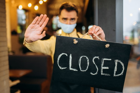 CLOSED. Sad waiter, barista or small business owner. Defocused guy in a medical protective mask and...