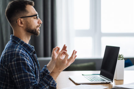 Satisfied caucasian busy freelancer is meditate at the workplace. Calm male employee takes a break from work online. Distant work or learningの写真素材