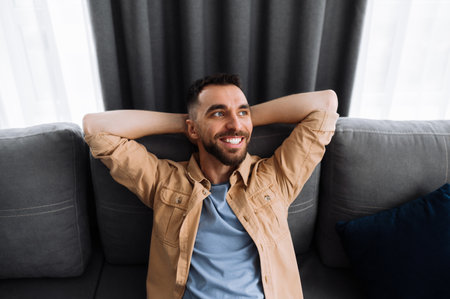 Portrait of a happy calm caucasian man sitting on the sofa, in the end of working day, resting from tense work, dreaming about vacations and smilingの写真素材