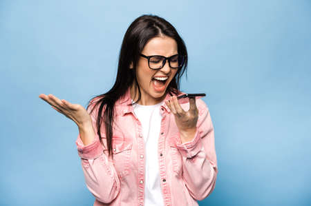 Angry emotional caucasian brunette woman shouting while talking on mobile phone with friends, family...