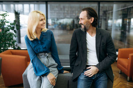 Joyful successful colleagues sitting on the sofa in office while break. Happy middle aged business people having a conversation, talking and discussing work process, communication conceptの写真素材