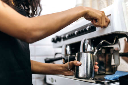 Close up photo of making coffee. Barista girl prepares coffee, pours milk for make a cappuccino using coffee machineの写真素材