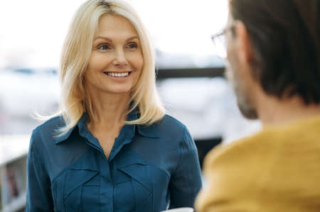 Attractive blonde-hair business woman having a conversation with male colleague, smiling. Middle...