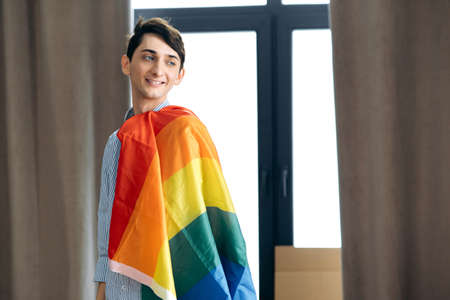 Homosexual guy. Young happy caucasian gay guy posing with colorful big lgbt flag looking to the side and smiling. Freedom concept for same sex couplesの写真素材