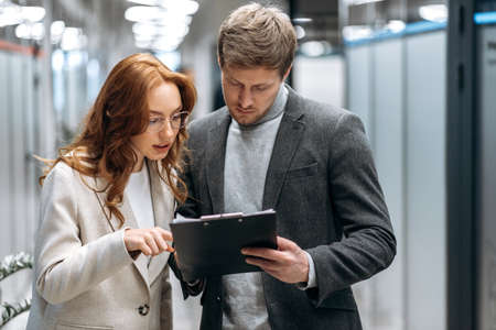 Focused young adult coworkers discussing new business plan, standing in office hall, working...