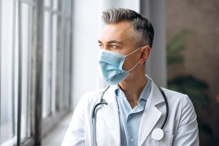 Portrait of a qualified middle-aged caucasian male doctor, in a medical uniform and a protective...
