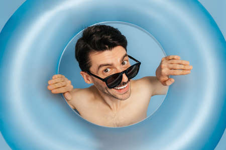 Close-up photo of a shirtless cheerful amazed caucasian young man in a sunglasses looks through...