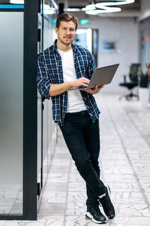 Caucasion male freelancer is standing in modern office, looking at the camera, smiling. Happy young...