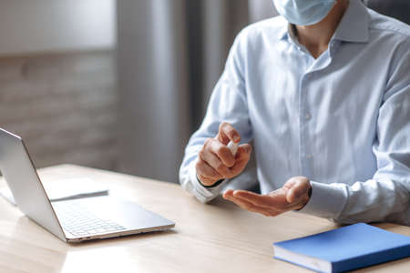 Caucasian man, office worker or manager, in a medical mask, sits at workplace, in formal wear,...