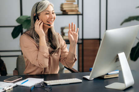 Successful confident senior Asian gray-haired female business lady, manager, coach, wearing headset,...