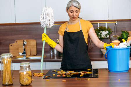 Disappointed, overworked, hardworking middle aged gray-haired Asian housewife or cleaning lady...